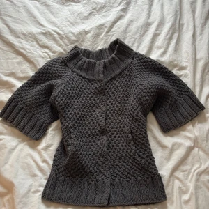 Grå stickad kofta från COS - Säljer en snygg grå stickad kofta från COS i storlek XS. Koftan har korta ärmar och knappar framtill. Perfekt för lager-på-lager under kyliga dagar.