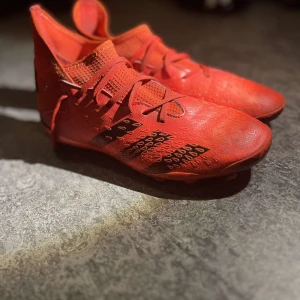 Röda fotbollsskor med snörning - Snygga röda fotbollsskor med snörning och mönstrad yta. Skorna har dobbar för bra grepp på planen och en modern design som sticker ut.