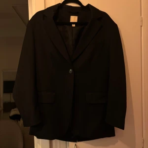 Svart kavaj - Oversized snygg svart kavaj med klassisk design och enkelknäppning. Passar bra till både vardag och festliga tillfällen. Säljer pågrund av att den inte kommer till användning. 