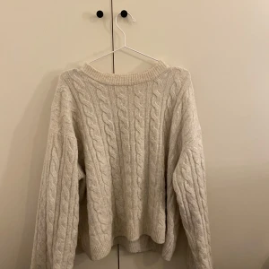 Beige stickad tröja - Mysig beige stickad tröja med kabelstickat mönster. Perfekt för kyliga dagar med sin avslappnade passform och långa ärmar.
