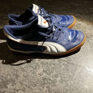 Blå och vita Puma sneakers - Snygga blå och vita sneakers från Puma med klassisk design. Skorna har en vit sula och snörning framtill. Perfekta för en sportig look.