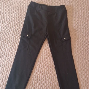 Svarta cargopants med fickor - Snygga svarta cargopants med praktiska fickor på sidorna. Byxorna har en tight passform och är perfekta för en avslappnad stil. De har knappar på fickorna för extra säkerhet.