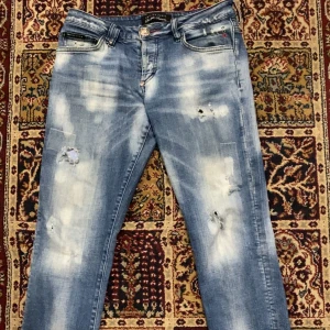 Blå jeans med slitningar från Philipp Plein - Snygga blå jeans med slitningar och blekta detaljer från Philipp Plein. Byxorna har en normal passform och är dekorerade med broderad text på bakfickan. Perfekta för en trendig look.