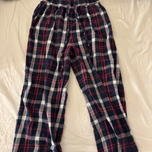 Rutig pyjamasbyxa - Mysiga pyjamasbyxor med rutig design i blått, vitt och rött. Byxorna har en elastisk midja med snörning för extra komfort. Perfekta för en avslappnad dag hemma.