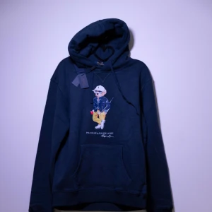 Ralph Lauren Hoodie - Helt ny Ralph Lauren Hoodie med en ikonisk nallebrodyr på framsidan. Hoodien har en klassisk passform med justerbar huva och en praktisk magficka. Perfekt för en avslappnad stil. Fler storlekar finns i min profil😊