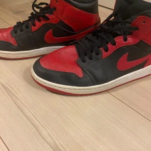 Nike Air Jordans - Snygga Nike Air Jordans i svart och röd färgkombination. Skorna har en hög modell, perfekt för dig som vill ha en stilren och sportig look.