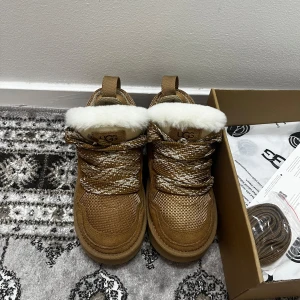 Chestnut uggs lowmel - Säljer ett par bruna boots från UGG med vit pälsfoder och snörning. Perfekta för kalla dagar med sin robusta sula och varma insida. Skorna har en snygg och praktisk design som passar bra till vinterns alla äventyr.