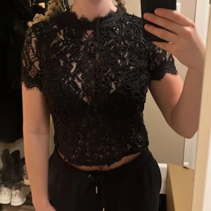 Svart spetsblus Zara - Snygg svart spetsblus med korta ärmar och ett vackert blommönster. Blusen är croppad och har en elegant design som passar perfekt för festliga tillfällen.