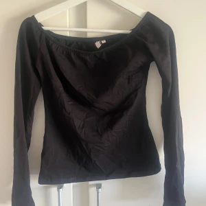 Svart långärmad topp från Nelly - Snygg svart långärmad topp från Nelly med en offshoulder-design. Perfekt för en stilren look. Toppen är i ett mjukt material som sitter bekvämt.