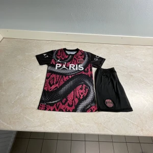 PSG special mbappé tröja - Snygg PSG fotbollströja från Nike i svart och rosa med ormmönster. Tröjan har korta ärmar och klubbens emblem på bröstet. Namnet och numret 'Mbappé 7' pryder baksidan. Perfekt för fans av Paris Saint-Germain! Special edition.