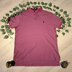 Rosa randig pikétröja från Ralph Lauren - Säljer en snygg rosa pikétröja från Ralph Lauren med vita ränder. Tröjan har en klassisk krage och korta ärmar. Perfekt för en stilren look. 