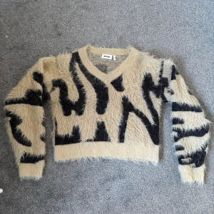 Beige och svart tröja från weekday  - Säljer en unik och fluffig beige tröja från Weekday med svart zebramönster. Tröjan har en v-ringad design och långa ärmar. Skön och sticks inte.