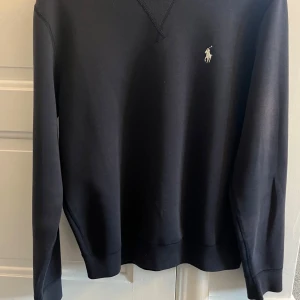 Svart tröja från Polo Ralph Lauren - Säljer en stilren mörkblå tröja från Polo Ralph Lauren med deras ikoniska logga på bröstet. Tröjan har långa ärmar och en klassisk passform. Perfekt för en avslappnad och snygg look.