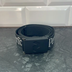 Svart bälte från peak performance  - Snyggt svart bälte från peak performance och en stilren svart spänne. Bältet är justerbart och är 105 cm, perfekt för att ge din outfit en cool touch ✅