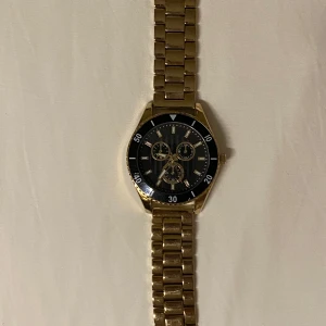 Guldfärgad klocka - Stilren guldfärgad klocka med svart urtavla och tre mindre urtavlor för extra funktioner. Klockan har en klassisk länkarmband i guld och tydliga markeringar på ringen. Perfekt för den som vill ha en elegant och funktionell accessoar. Priset går att diskutera även om den inte är hugget i sten:)