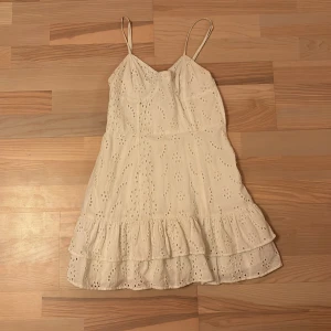 Vit klänning från Bershka - Söt vit klänning från Bershka med smala axelband och volangdetaljer. Klänningen har ett broderat mönster och är perfekt för varma dagar. Den är kort och har en luftig passform.