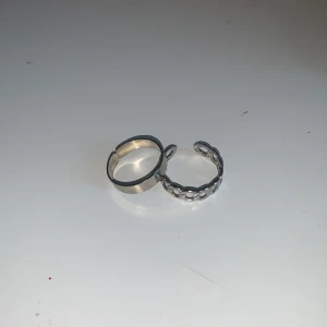 Två silverringar - Säljer två stilrena silverringar. Den ena har en slät yta medan den andra har en kedjedesign. Perfekta för att bära tillsammans eller separat för en minimalistisk look.