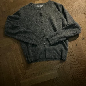 Grå kofta från Zara - Säljer en stilren grå kofta från Zara med knappar framtill. Perfekt för kyligare dagar och lätt att matcha med olika outfits. Koftan har långa ärmar och en mjuk textur.
