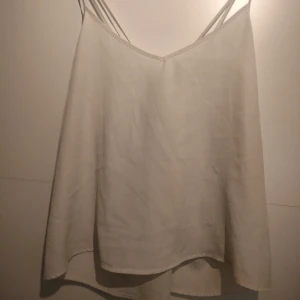 Vit linne från Hollister - Säljer en stilren vit linne från Hollister med dubbla axelband och en luftig passform. Perfekt för varma dagar eller som ett lager under en kavaj. Toppen har en enkel och elegant design som passar till många olika stilar. Storlek L.