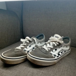 Vans sneakers med schackmönster - Snygga Vans sneakers med klassiskt svartvitt schackmönster och grå mockadetaljer. Skorna har vit snörning och den ikoniska 'Off the Wall'-loggan på hälen. Perfekta för en avslappnad stil.