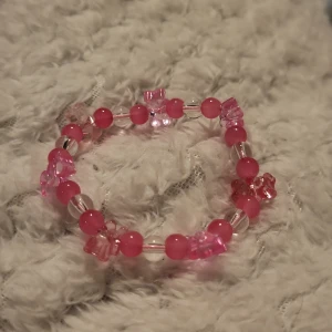 Rosa pärlarmband med blommor - Charmigt rosa armband med pärlor och blommor. Armbandet har en elastisk tråd för enkel passform och är dekorerat med små blommor i olika nyanser av rosa. Perfekt för att lägga till en färgglad touch till din stil.