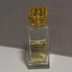 Parfym L'Amour de Soi från Leojuliane - Elegant parfymflaska med en lyxig guldkrona som lock. Flaskan är rektangulär och genomskinlig, vilket visar den ljusgula vätskan inuti. Perfekt för den som vill ha en doft med stil och elegans.
