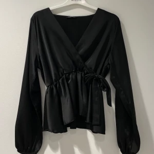 Svart omlottblus med knytband - Super snygg blus från missay. Blusen har en elegant knytning vid midjan. Passar till flera olika tillfällen. Använd fåtals gånger. 