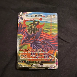 Pokémonkort VMAX - Säljer ett Pokémonkort med VMAX-design. Kortet har en färgglad framsida med en kraftfull illustration och japansk text. Baksidan har den klassiska Pokémon-designen med en pokéboll i mitten. Perfekt för samlare eller Pokémon-fans!