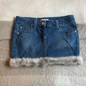 Jeanskjol med pälsdetalj från Blugirl - Trendig jeanskjol från Blugirl med unik pälsdetalj längs nederkanten. Kjolen har klassiska femficksdesign och en snygg blå denimfärg. Perfekt för att ge din outfit en cool touch.