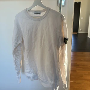 Vit långärmad tröja från Stone Island - Säljer en stilren vit långärmad tröja från Stone Island. Tröjan har en rund halsringning och det ikoniska Stone Island-märket på ärmen. Perfekt för en avslappnad och trendig look.