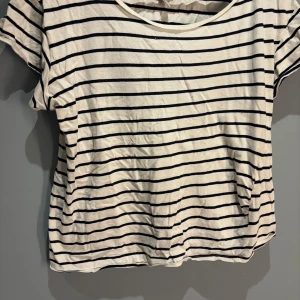 Randig t-shirt från H&M - Säljer en klassisk randig t-shirt från H&M i svart och vit. Den har en rund halsringning och korta ärmar, perfekt för en avslappnad stil. Tillverkad i mjuk bomull för extra komfort.