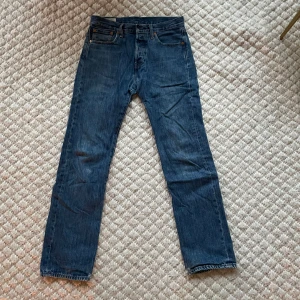 Blå Levis 501 jeans - Klassiska blå Levis 501 jeans med rak passform och knappgylf. Perfekta för en avslappnad stil. Tillverkade i slitstarkt denim. Nypris 1200. Lite slitna längd nere på jeansen.