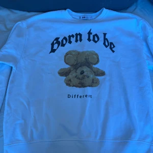 Vit sweatshirt med nalletryck - Säljer en vit sweatshirt med texten 'Born to be Different' och ett nalletryck på framsidan. Tröjan har långa ärmar och en rund halsringning. Perfekt för en avslappnad stil.