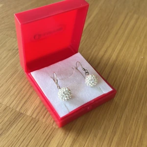 Gllittriga örhängen i silver - ”Discoboll”-örhängen i silver med små gnistrande stenar (kristall enligt guldfynds hemsida) som är snygga till fest eller andra tillfällen. Säljer då jag inte använder silver. Örhängena är noga tvättade och disinfekterade, och kommer i sin orginalbox. Nypris: 398kr