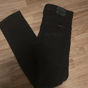 Nudie Jeans - Säljer ett par svarta Lean Dean jeans från Nudie Jeans. De är tillverkade i 99% ekologisk bomull och 1% elastan för en bekväm passform. Modellen är slim och heter lean dean och färgen är 'Dry Ever Black'. Perfekta för en stilren look.