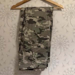 Camouflage cargobyxor från Lindex - Snygga camouflage cargobyxor från Lindex med flera knappar och praktiska fickor. Perfekta för en avslappnad stil med en touch av edge. Byxorna har en klassisk camo-look i gröna och beige toner.