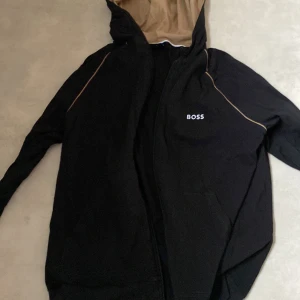 Svart jacka från Boss - Snygg svart jacka från Boss med beige foder och dragkedja. Perfekt för en stilren look.