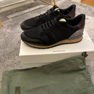 Valentino rockrunner - Snygga svarta sneakers från Valentino med detaljer i brunt och grått. Skorna har en klassisk snörning och en bekväm sula. Perfekta för en stilren look. Två dustbags tillkommer, storlek 41, kom privat för fler frågor eller bilder!