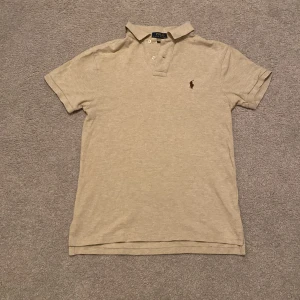 Beige pikétröja från Ralph Lauren - Snygg beige pikétröja från Ralph Lauren i slim fit. Tröjan har korta ärmar och en klassisk krage med knappar. Fint skick utan några stora defekter. Perfekt för en stilren look!