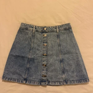 Jeanskjol med knappar - Trendig jeanskjol i kort med knappar framtill. Perfekt för en avslappnad stil. Kjolen har bälteshällor och en klassisk blå jeansfärg.