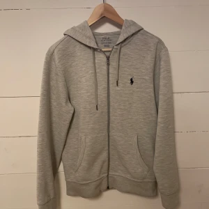 Grå hoodie från Ralph Lauren - Säljer en stilren grå hoodie från Ralph Lauren med dragkedja och justerbar huva. 10/10 skick, ny pris 2295kr. Mitt pris 899 kr
