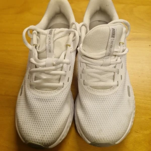 Vita Nike sneakers - Säljer ett par vita Nike sneakers med snörning. Skorna har en stilren design med en vit sula och Nike-logga på sidan. Perfekta för en sportig look.