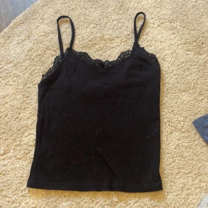 Svart ribbad linnetopp från H&M - Snygg svart ribbad linnetopp från H&M med spetsdetaljer vid halsringningen. Perfekt för lager-på-lager eller som den är. Enkelt och stilrent plagg för många tillfällen.