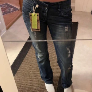 Blå jeans med slitningar lågmidjad 28/32 - Snygga blå jeans med slitningar och en klassisk femficksdesign. De har en normal passform och är perfekta för en avslappnad stil. Jeansen har en knappgylf och är tillverkade i ett slitstarkt denimtyg.