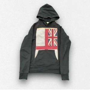 Mörkgrå hoodie från Ralph Lauren - Säljer en snygg mörkgrå hoodie från Ralph Lauren med en stor flaggdesign på framsidan. Jag är 178 och väger 70 kg och den sitter tajt på mig. Säljer för att den är för liten.