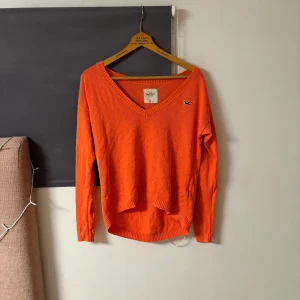Orange tröja från Hollister - Säljer en snygg orange tröja från Hollister med v-ringning och ribbade kanter. Tröjan har en liten logga på bröstet och är perfekt för en avslappnad stil. Passar bra till jeans eller kjol. 🧡