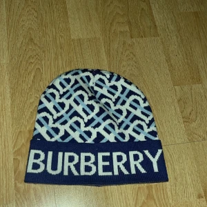  mössa från Burberry - Snygg mössa från Burberry med ett stilrent mönster i blått och vitt. Mössan har en bred kant med Burberry-loggan i stora bokstäver. Perfekt för att hålla sig varm med stil. Har bara testat den 