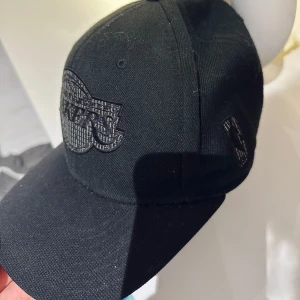 Svart keps från Mitchell & Ness - Snygg svart keps från Mitchell & Ness med broderad logga framtill. Perfekt för en casual look. Justerbar passform för optimal komfort.