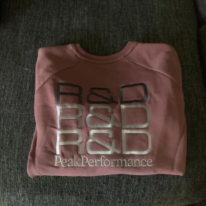 Rosa sweatshirt från Peak Performance - Säljer en snygg rosa sweatshirt från Peak Performance med tryck på bröstet. Tröjan har rund hals och långa ärmar, perfekt för en avslappnad stil. Sista bilden är lånad för att visa passform 
