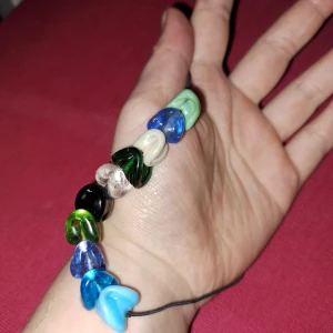 Färgglatt halsband med hjärtformade pärlor - Unikt halsband med hjärtformade pärlor i olika färger som blå, grön, svart och vit. Pärlorna är trädda på en svart snodd som ger en justerbar passform. Perfekt för att lägga till en färgglad touch till din stil.